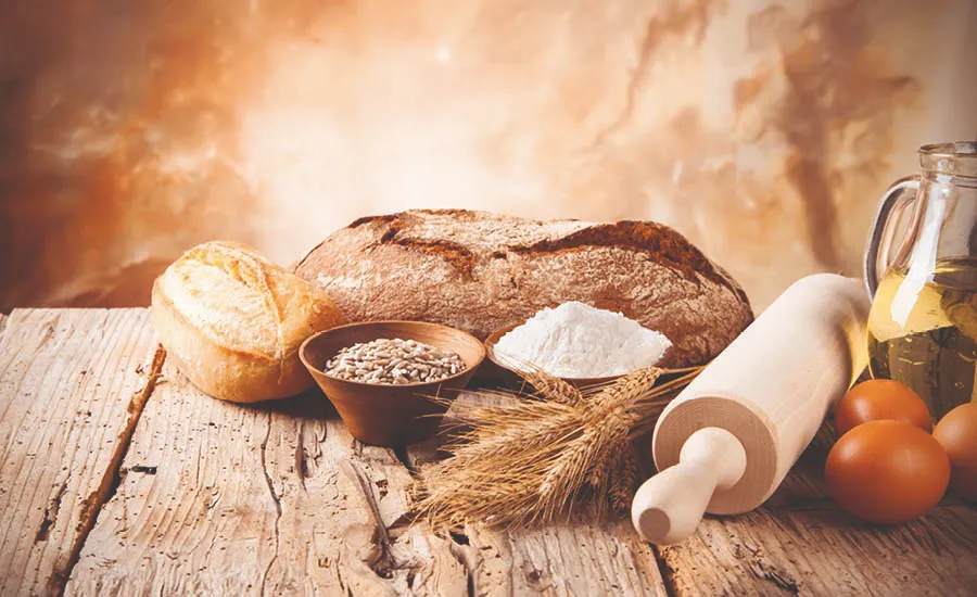 Brød, mel, korn og bakeingredienser på kjøkkenbenk med kjevle og olje